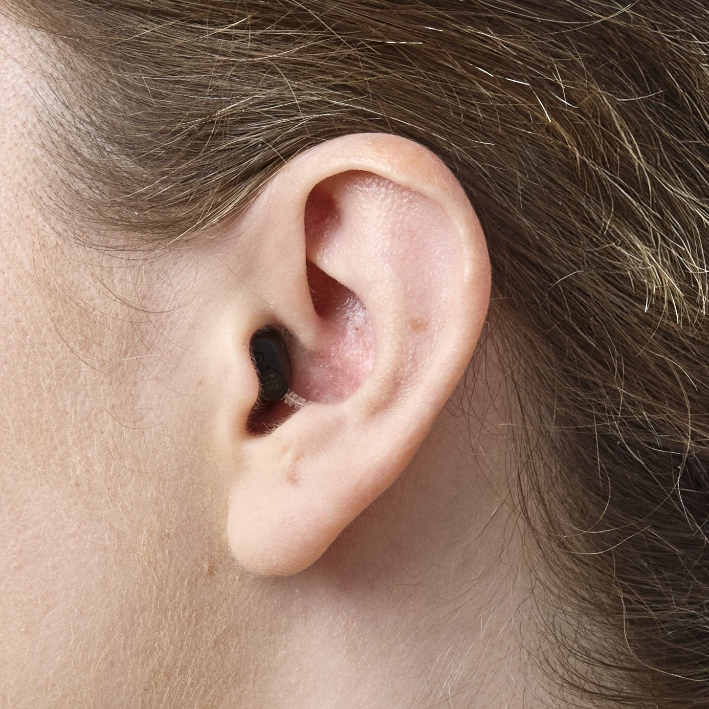 Close-up view of an Oticon Zeal NXT hearing aid worn in the ear of a woman — almost invisible from the side
